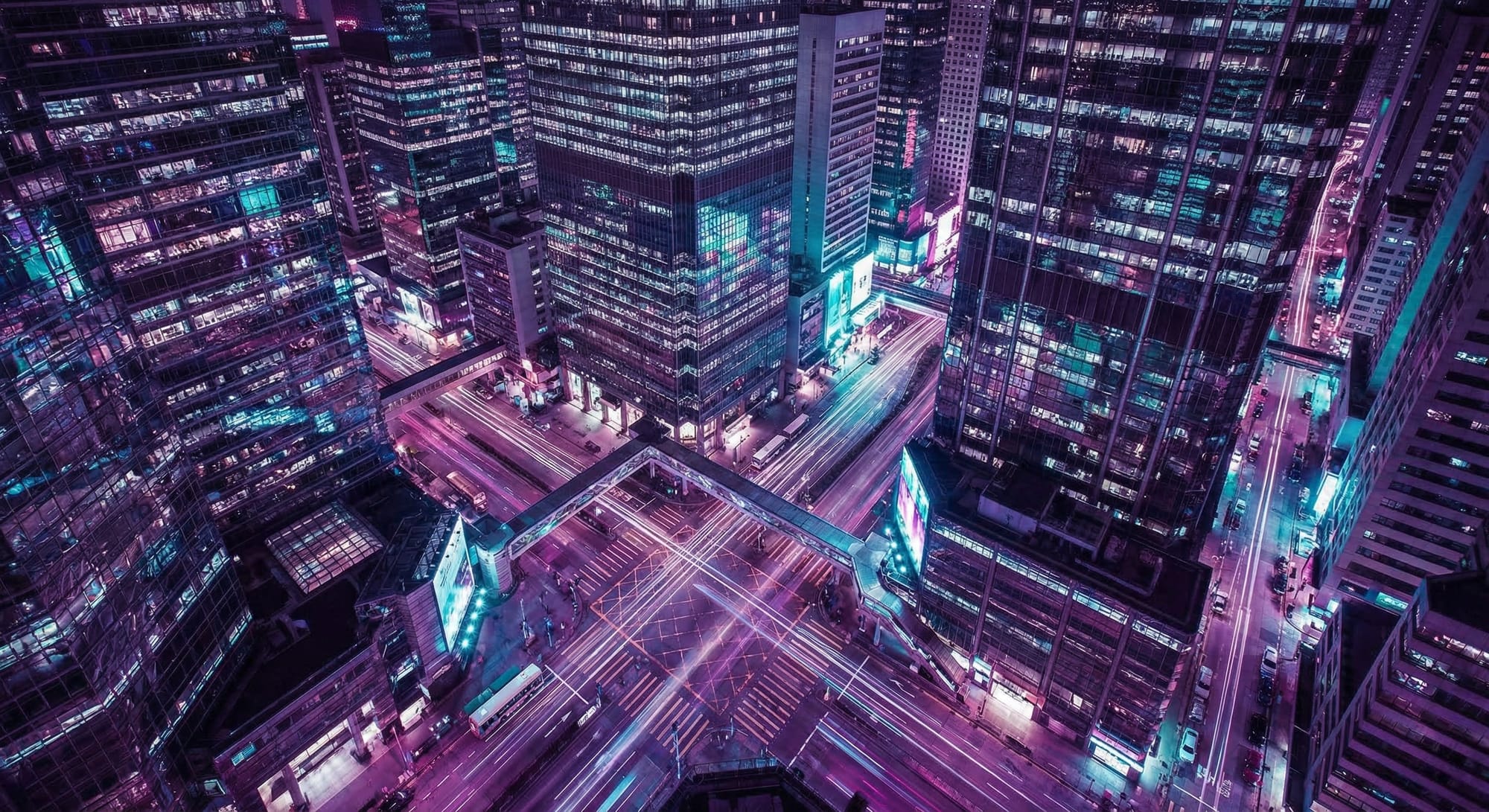 Luchtfoto van verlicht kruispunt omringd door hoge kantoorgebouwen met paarse en cyaan neonverlichting bij nacht