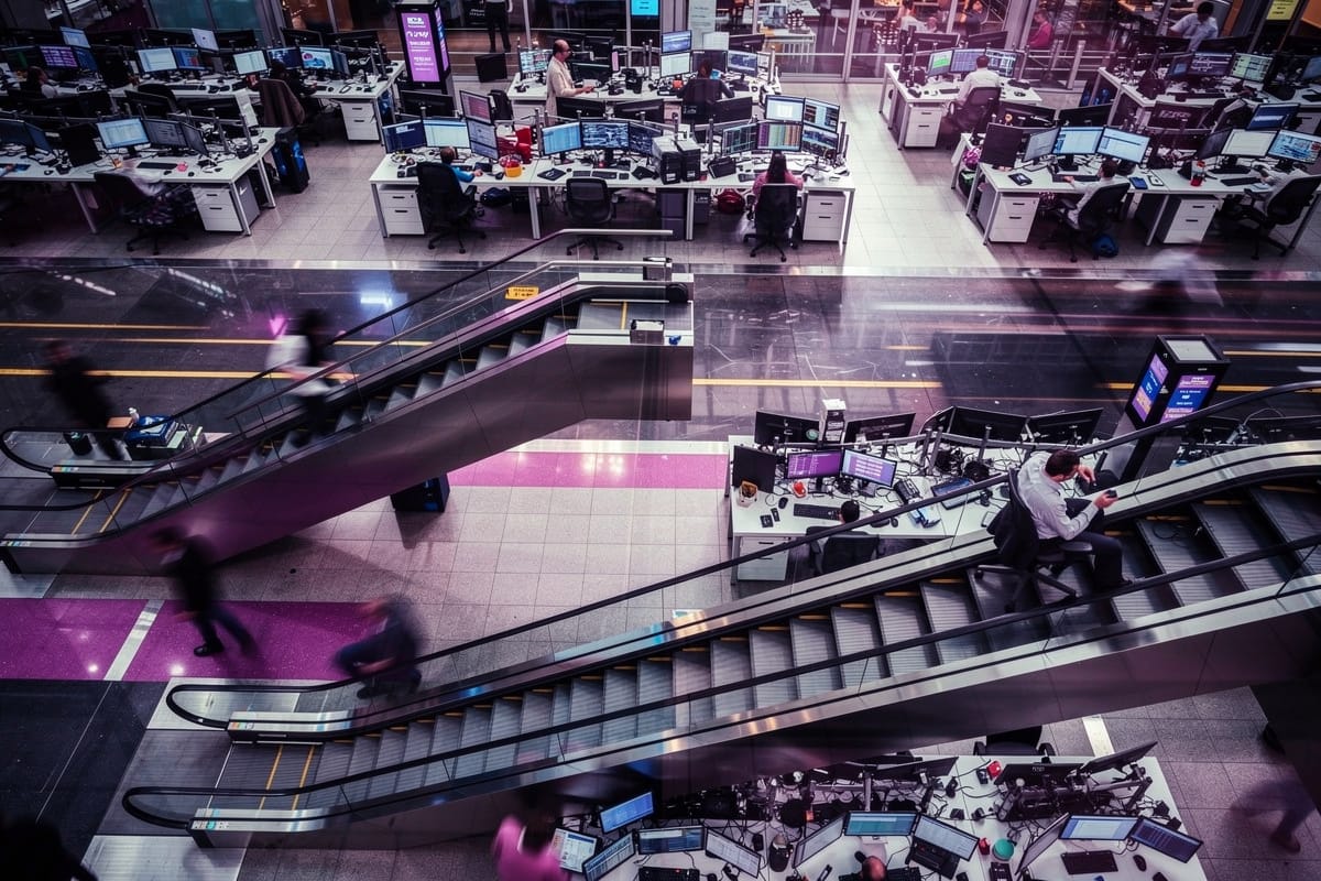 Overzichtsfoto van een modern kantoor met meerdere verdiepingen, roltrap, werkplekken met computerschermen en paarse vloeraccenten.
