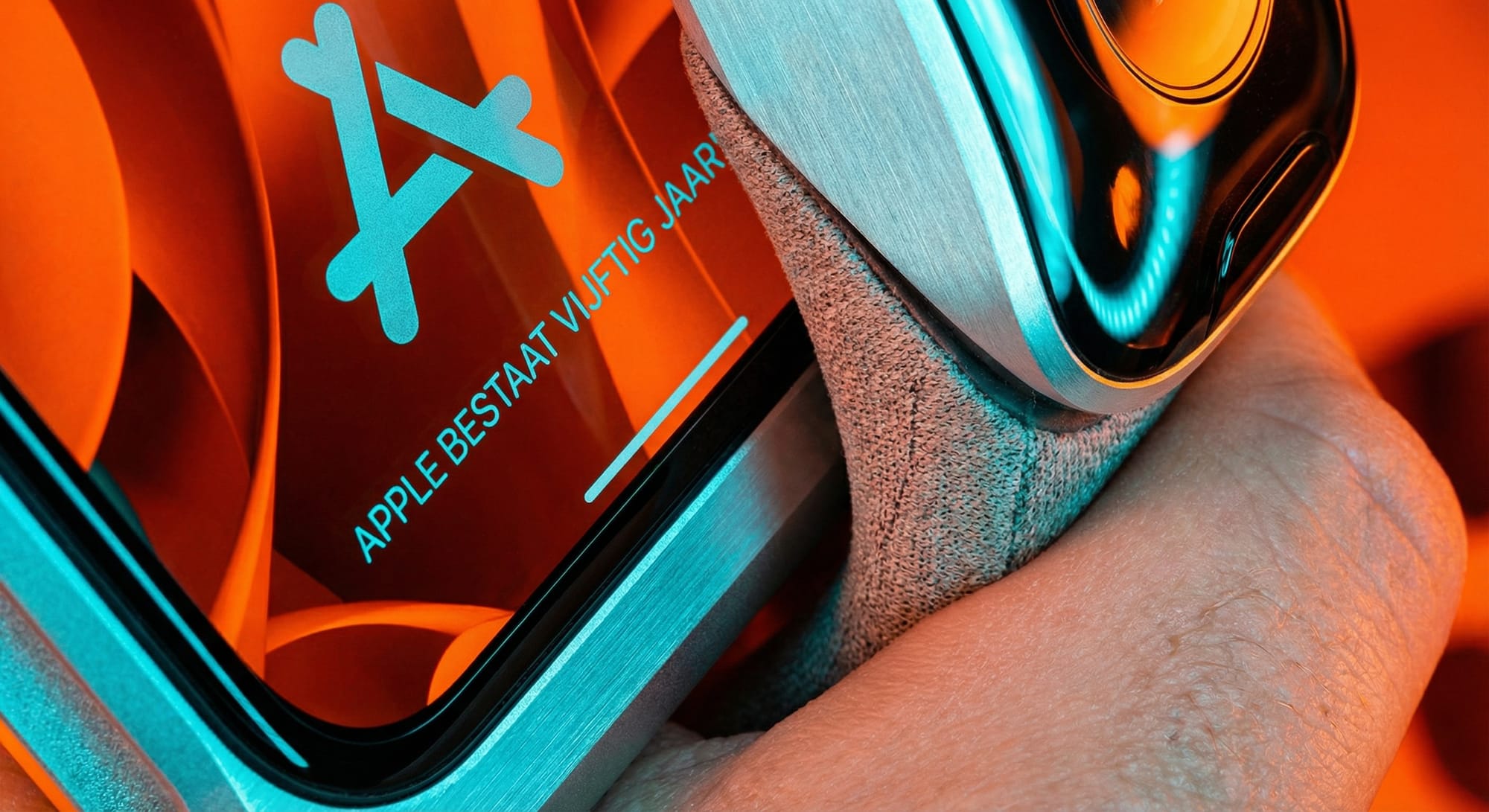 Apple-logo en tekst 'APPLE BESTAAT VIJFTIG JAAR' op oranje smartphone-scherm naast koptelefoon in turquoise en oranje tinten