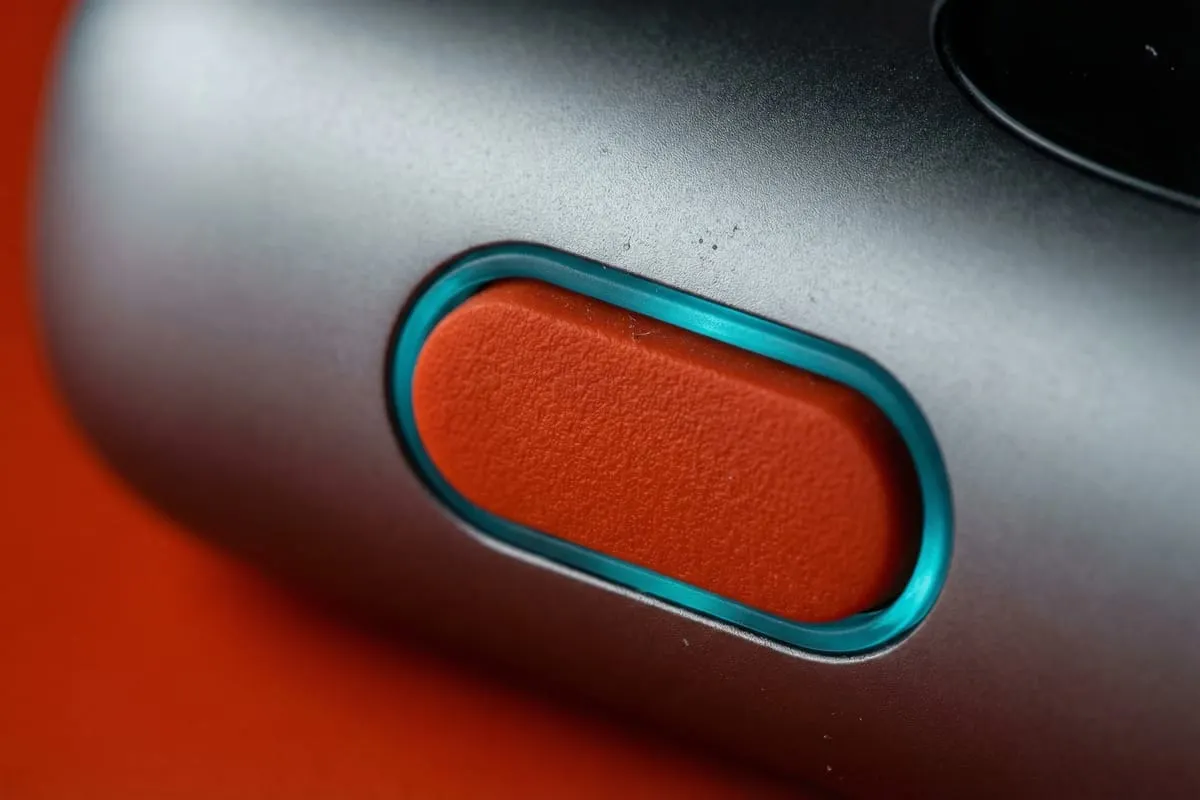 Close-up van een ovaal oranje detail met turquoise rand op een zilvergrijs metalen oppervlak