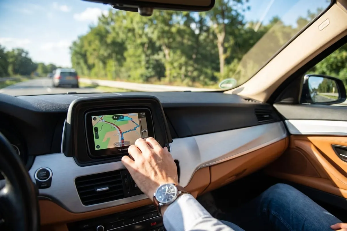 Hand met horloge bedient TomTom navigatiesysteem in auto-dashboard met oranje leren afwerking tijdens het rijden