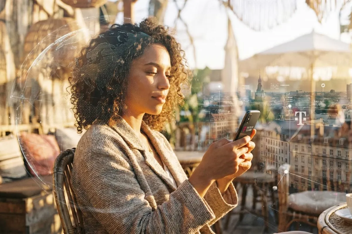 Vrouw met krullend haar gebruikt smartphone op balkon, digitale T-Mobile-logo overlay zichtbaar over stadsgezicht