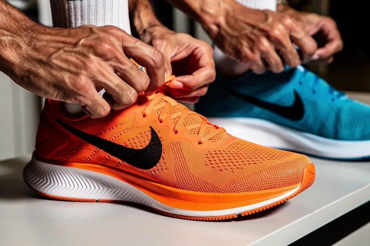 Handen van oudere persoon die veters van oranje Nike-hardloopschoen met zwart logo strikken