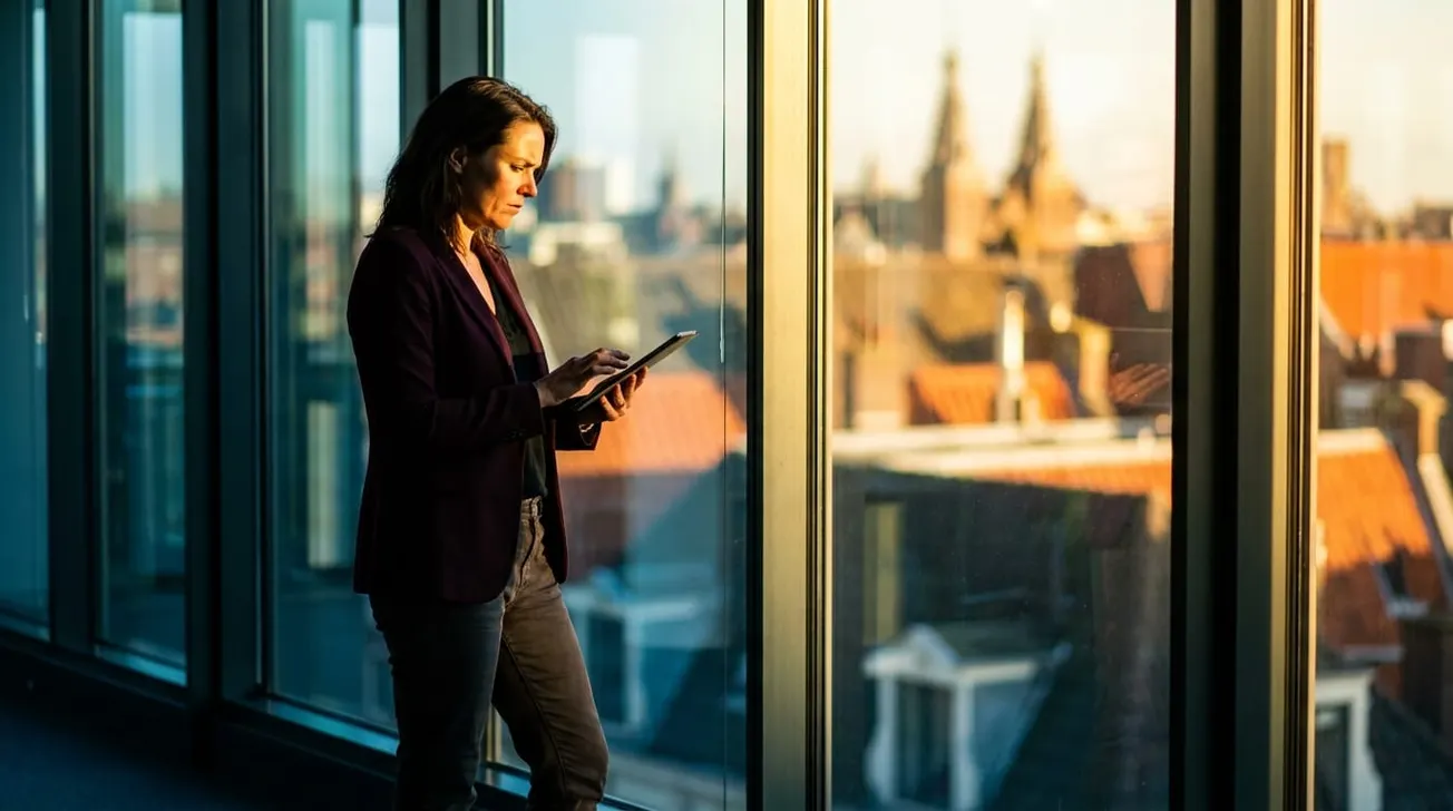 Vrouw in kantoor bekijkt tablet bij raam — strategische beslissing