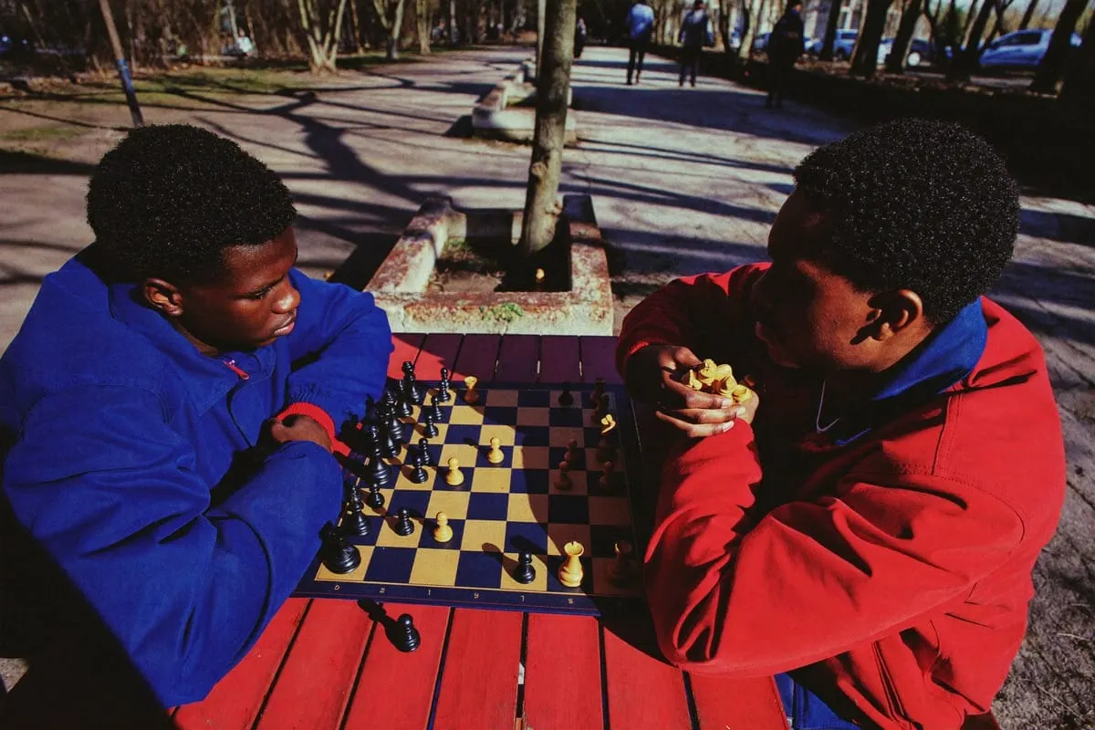 Twee jonge mannen in blauwe en rode jas spelen schaak aan een picknicktafel in een park