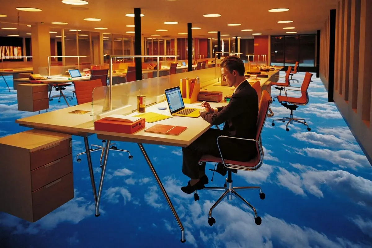 Man werkt aan laptop op kantoor dat zwevend boven wolkenlucht is gemonteerd, surrealistisch beeld