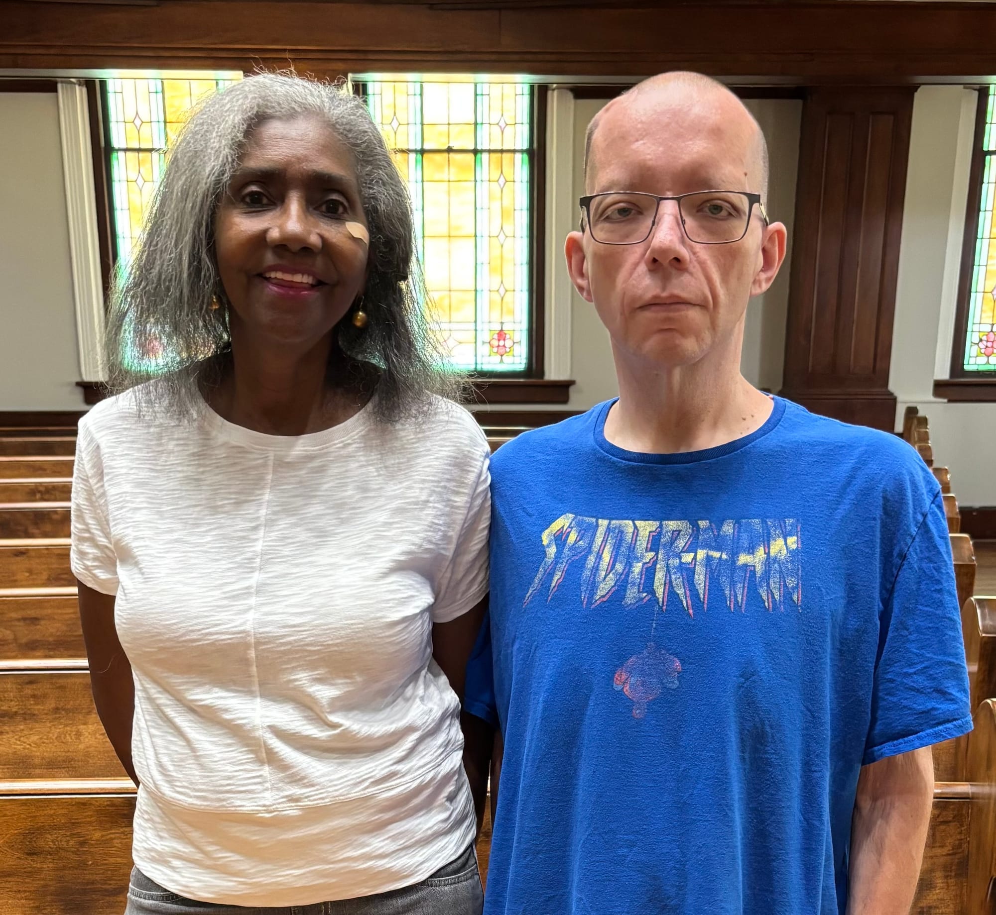 Residents of The Oaks -- Clarice Taylor and Keith Reid -- pose for a photo in the church's restored sanctuary. Clarice, aged 73, is a tall Black woman with gray hair. 47-year-old Keith is a white man with a shaved head and glasses.