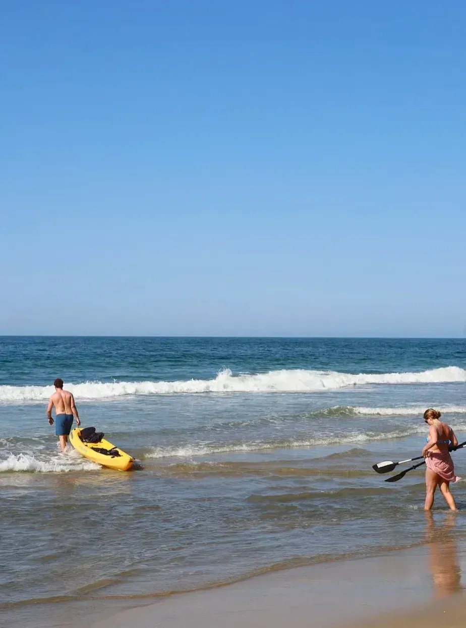 personas caminando en el mar con un kayak.