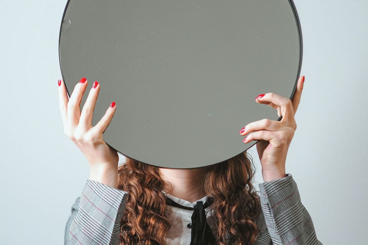 Woman hiding behind a mirror, inviting you to explore and reflect on your self-image and natural beauty.