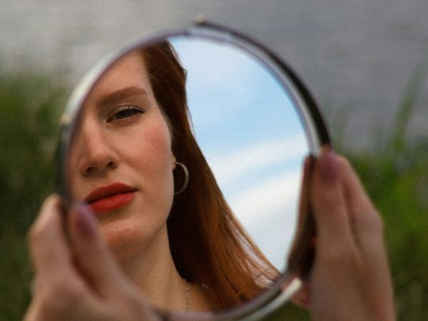 Woman holding a mirror, looking tired and concerned about her facial appearance, illustrating the desire for subtle, natural aesthetic rejuvenation.