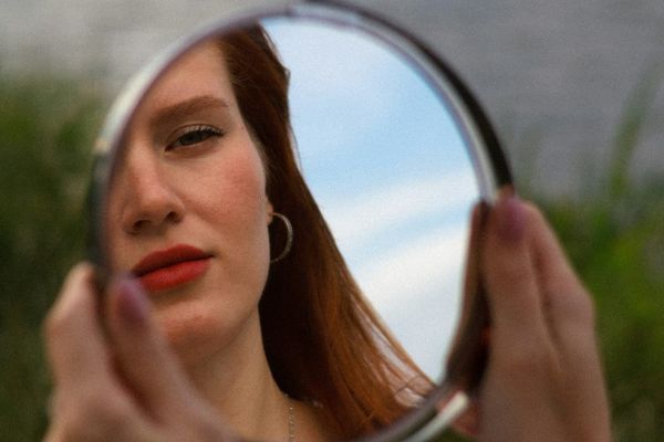Woman holding a mirror, looking tired and concerned about her facial appearance, illustrating the desire for subtle, natural aesthetic rejuvenation.