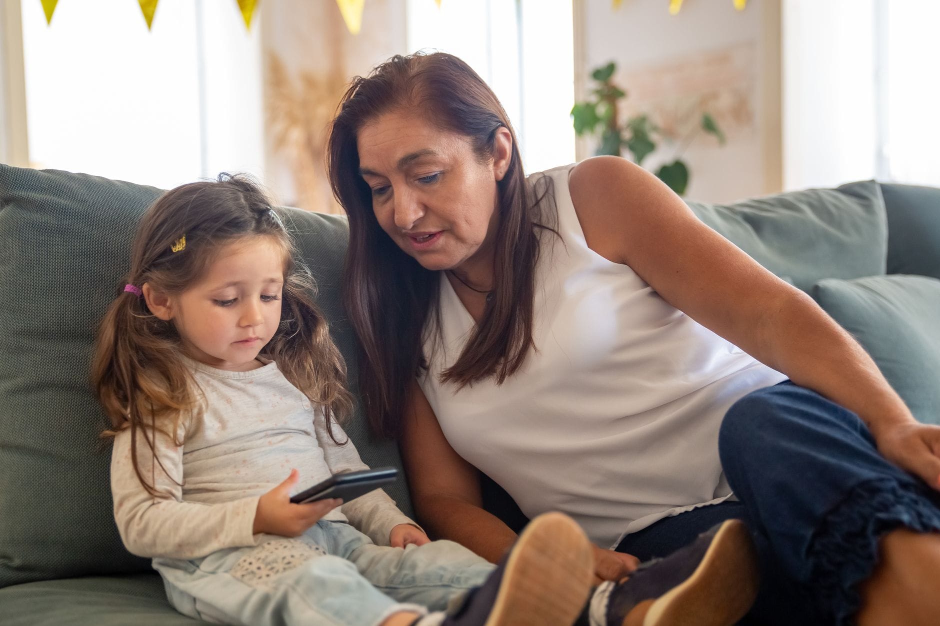 A grandmother and her granddaughter bonding over a smartphone while sitting on a cozy couch indoors.