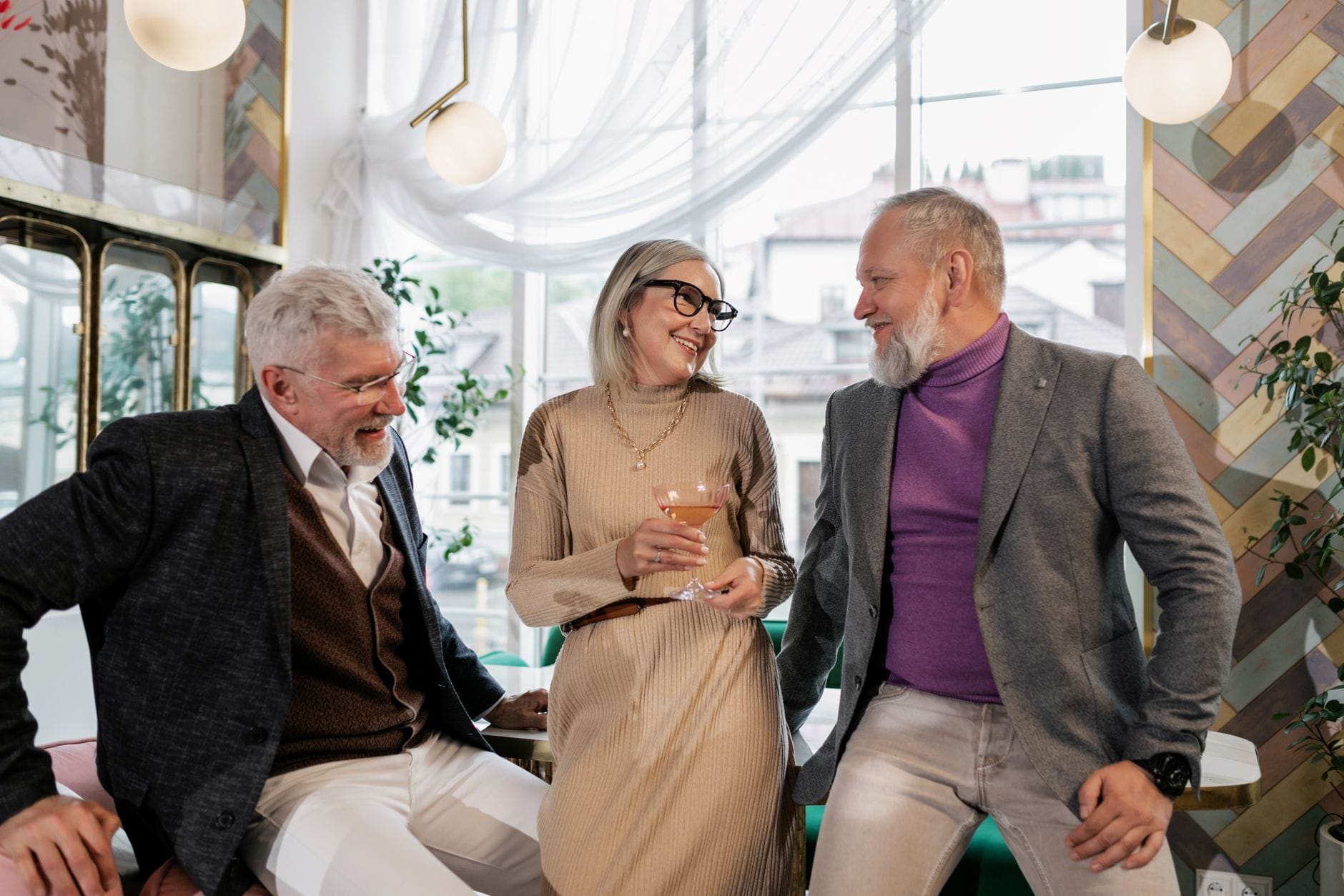 Three seniors bonding over drinks in a modern cafe setting, sharing laughter and joy.