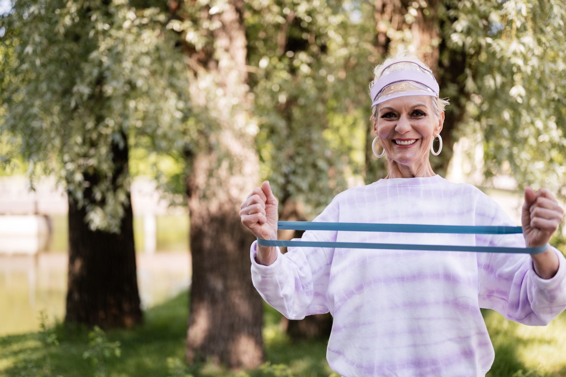 A cheerful senior woman engaging in fitness with a resistance band outdoors in a park setting.