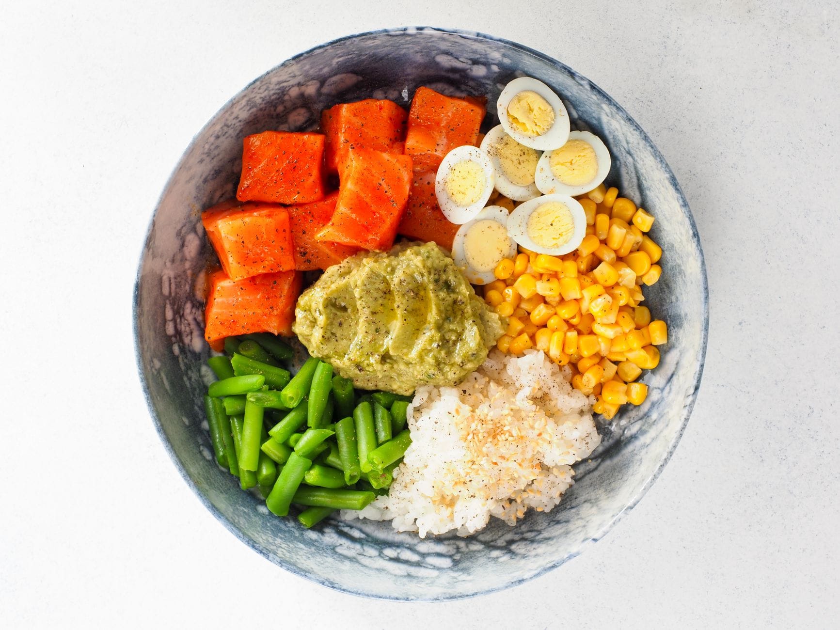 Top view of a colorful power bowl with salmon, eggs, and vegetables, perfect for healthy eating.