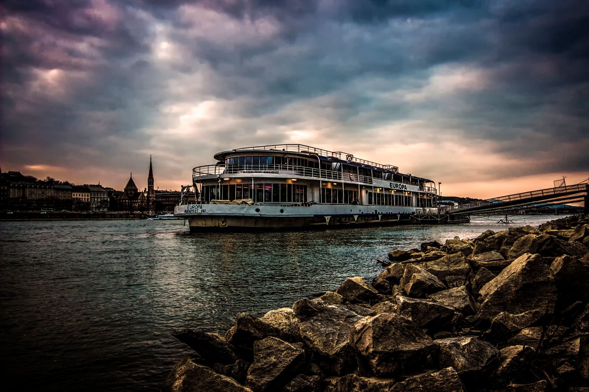 Luxurious river cruise ship sailing on the Danube in Budapest under a dramatic cloudy evening sky.