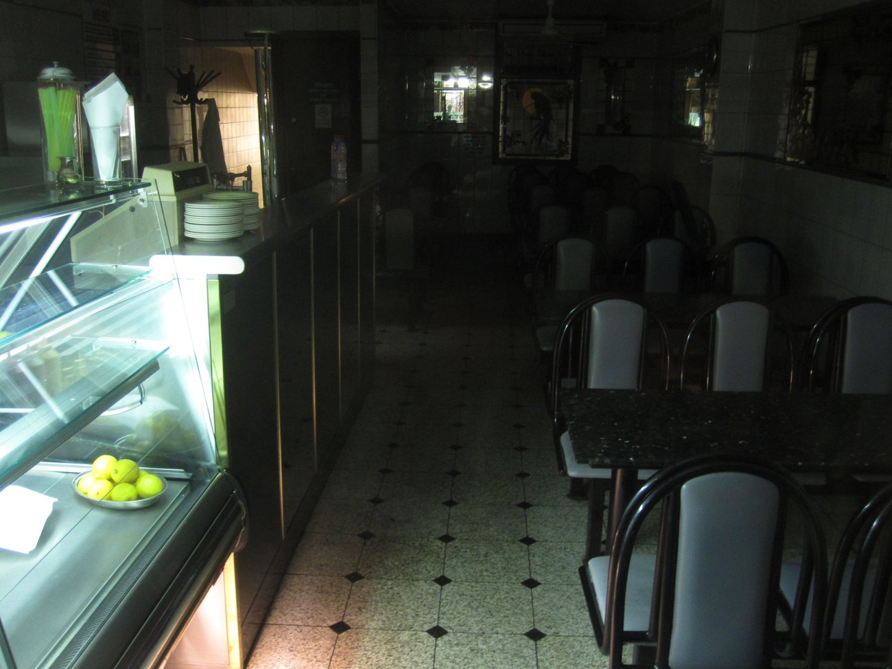An empty dark cafe at night. Lit only by the lights of the empty sandwich making station. 