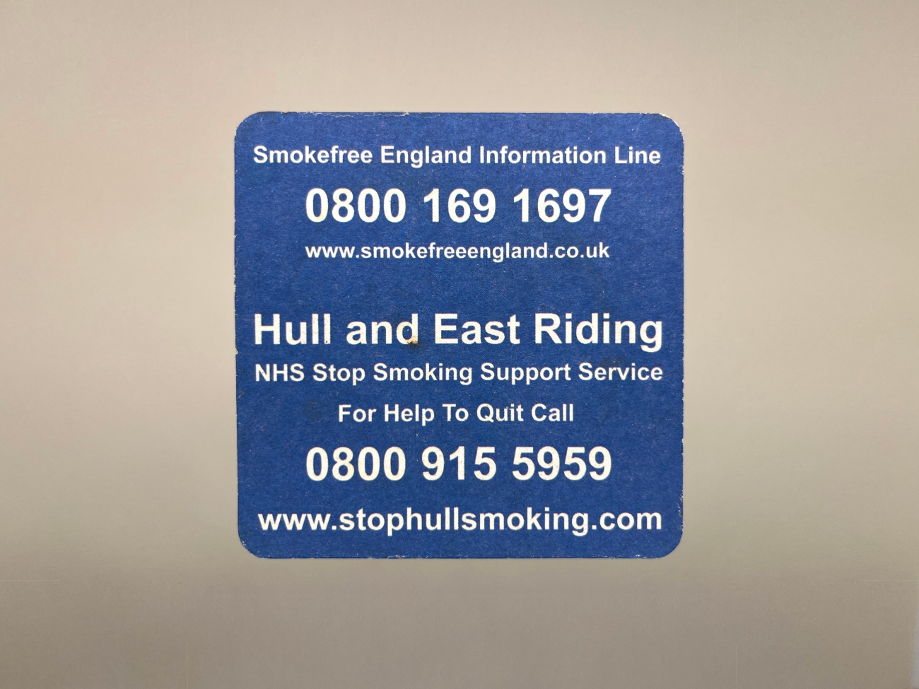 The rear of the blue beer mat with a smokefreeengland.co.uk website and information phone-number. Then another number for Hull and East Riding NJS stop smoking support services and a stophullsmoking.com URL