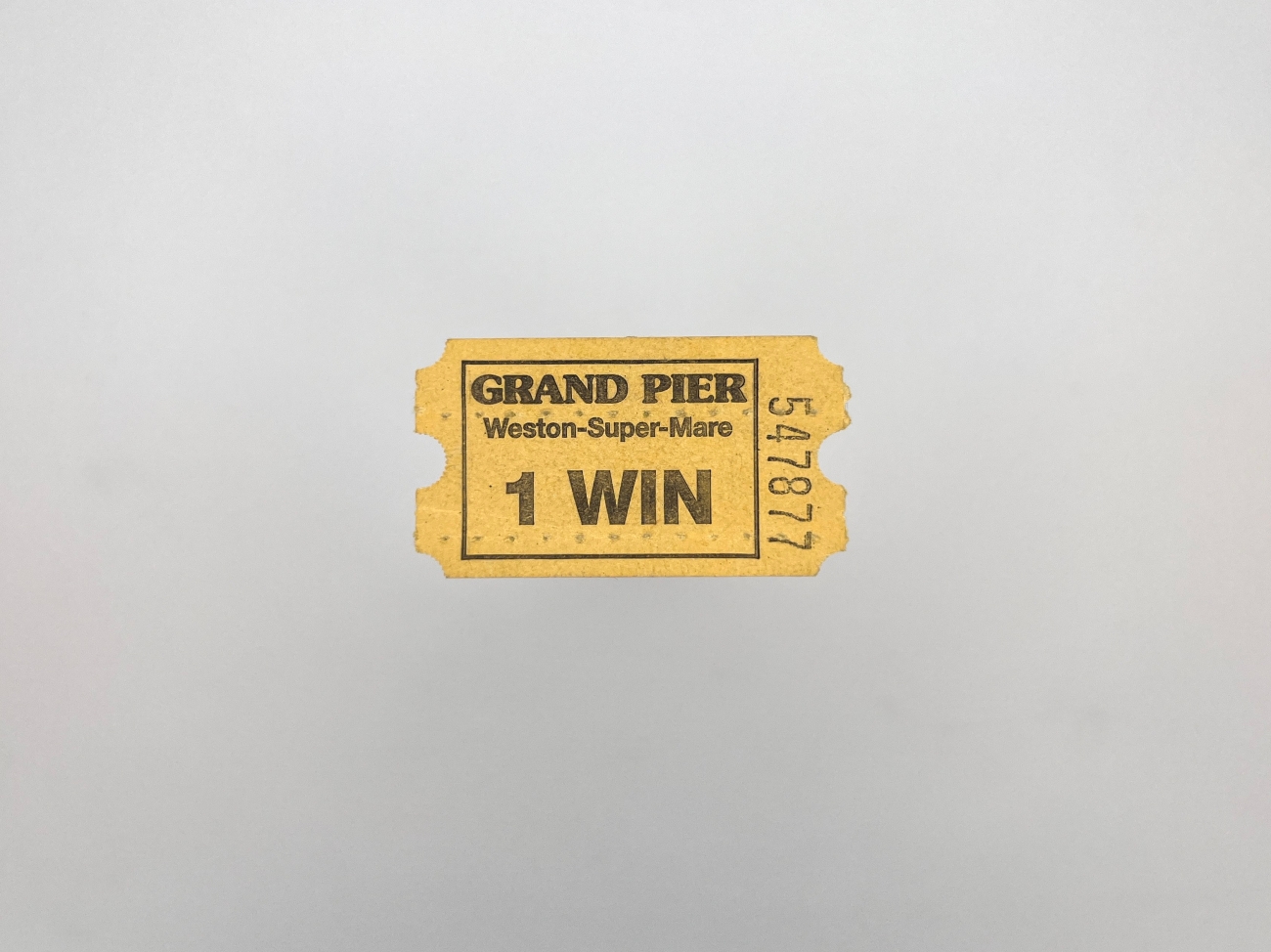 A small yellow paper ticket from a ticket machine. It says Grand Pier, Weston-Super-Mare 1 Win and has the serial number 547877 down the right side