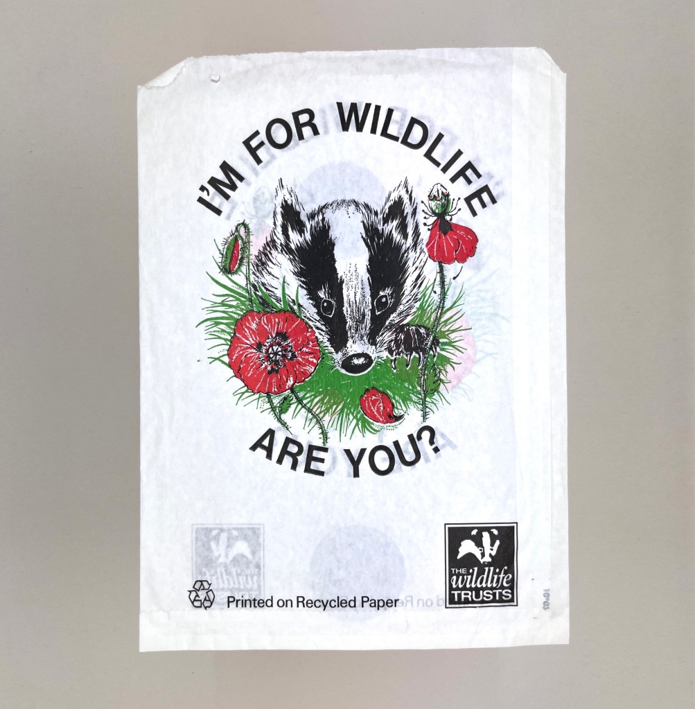 A white paper bag with a fairly realistic illustration of a badger on grass between some poppies. Above it says I'm For Wildlife. Below says Are You?