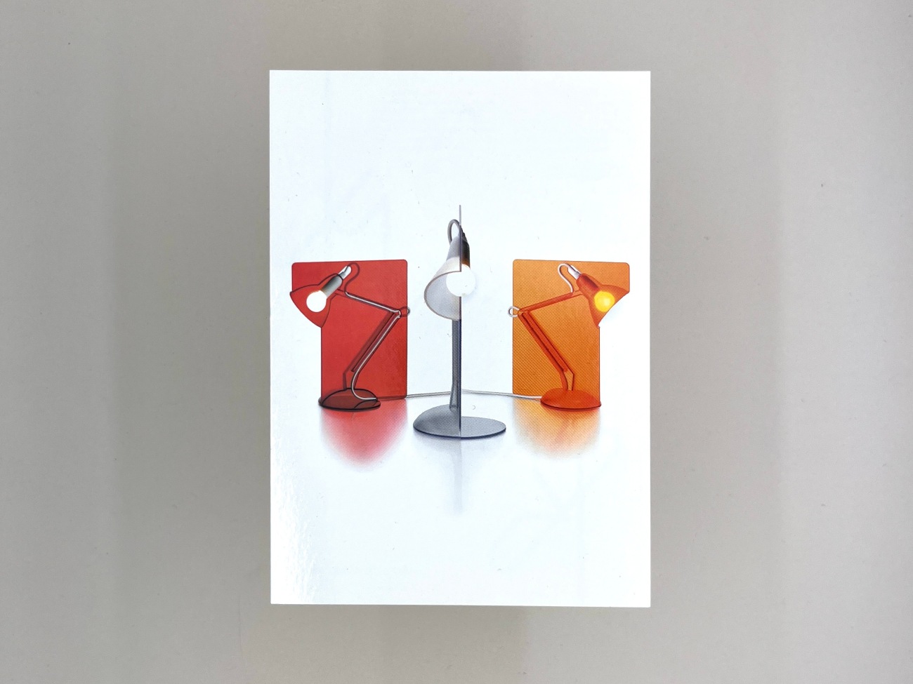 A postcard featuring three Anglepoise lamps (red, grey and orange) cast our of a sheet of plastic.  