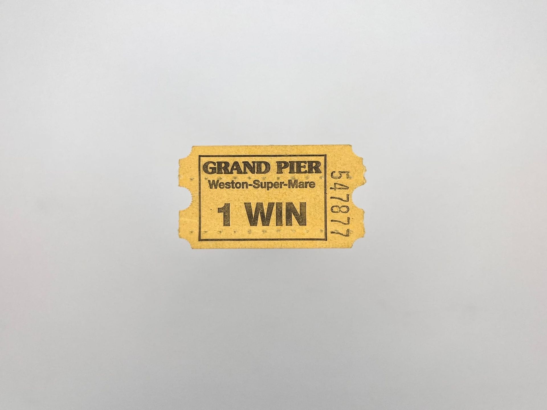 A small yellow paper ticket from a ticket machine. It says Grand Pier, Weston-Super-Mare 1 Win and has the serial number 547877 down the right side