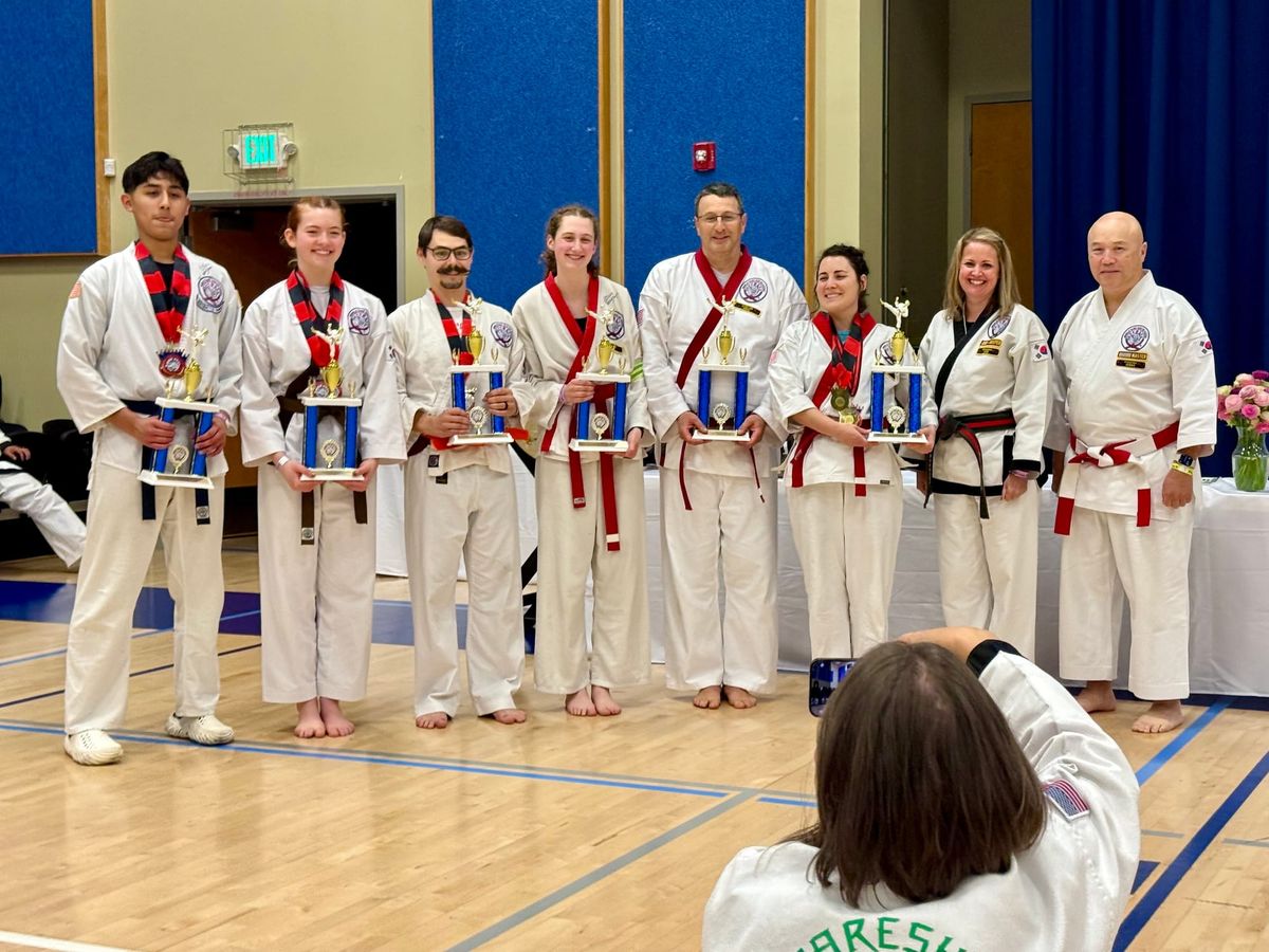 Lucia and Guy standing among a group of people holding trophies, Master Ohlson in the foreground taking their picture