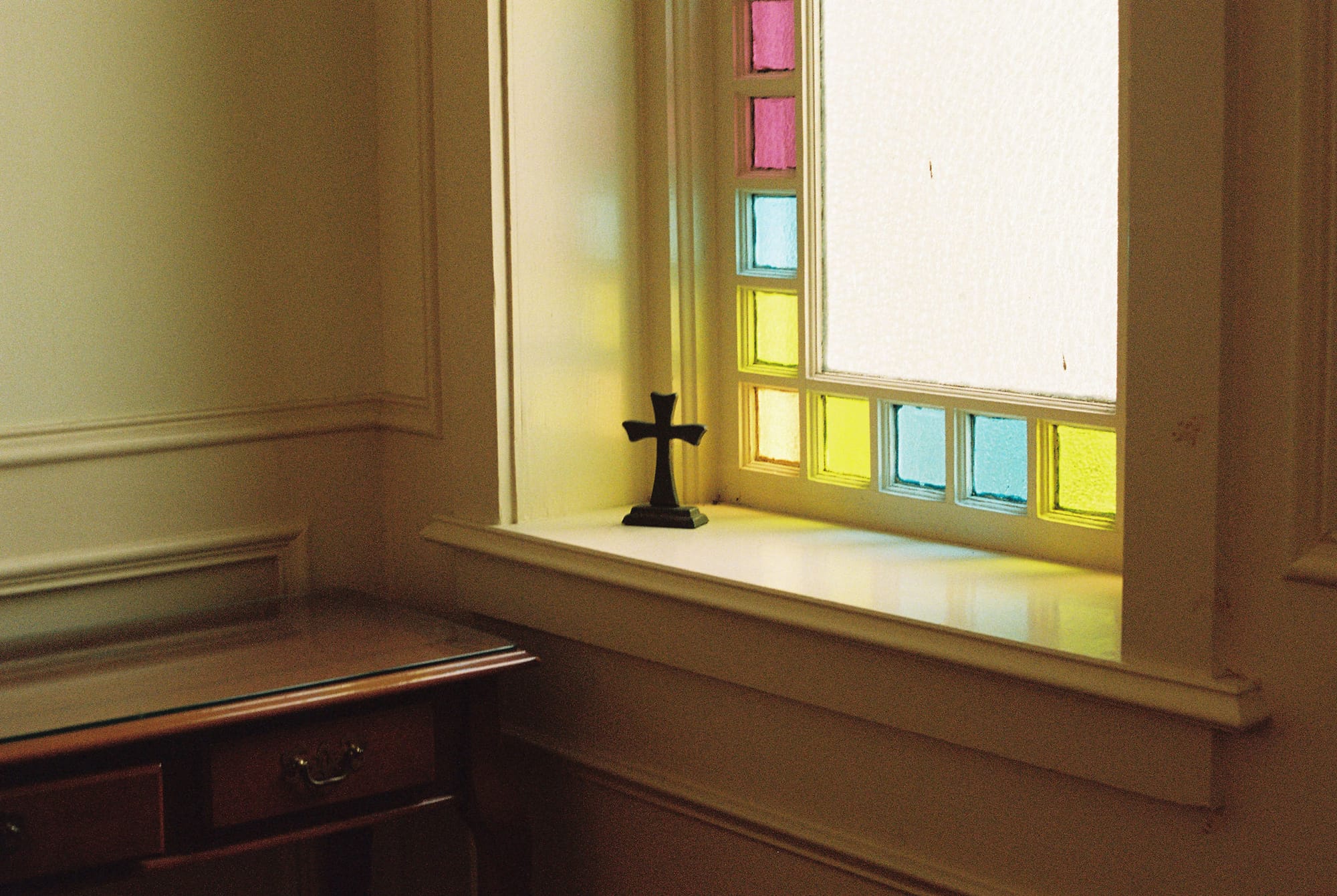 A small cross sitting on a windowsill in front of a stained glass window. 
