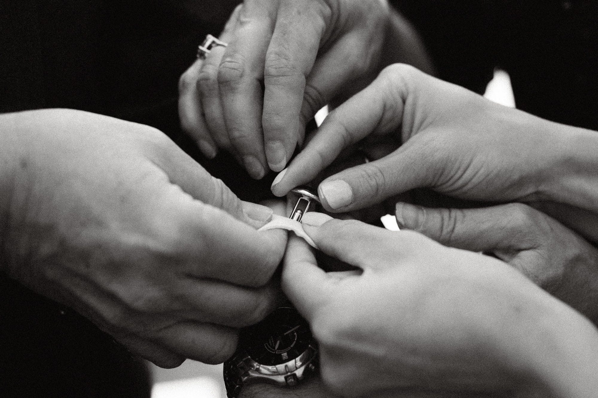 Several hands working together to put on a cufflink.