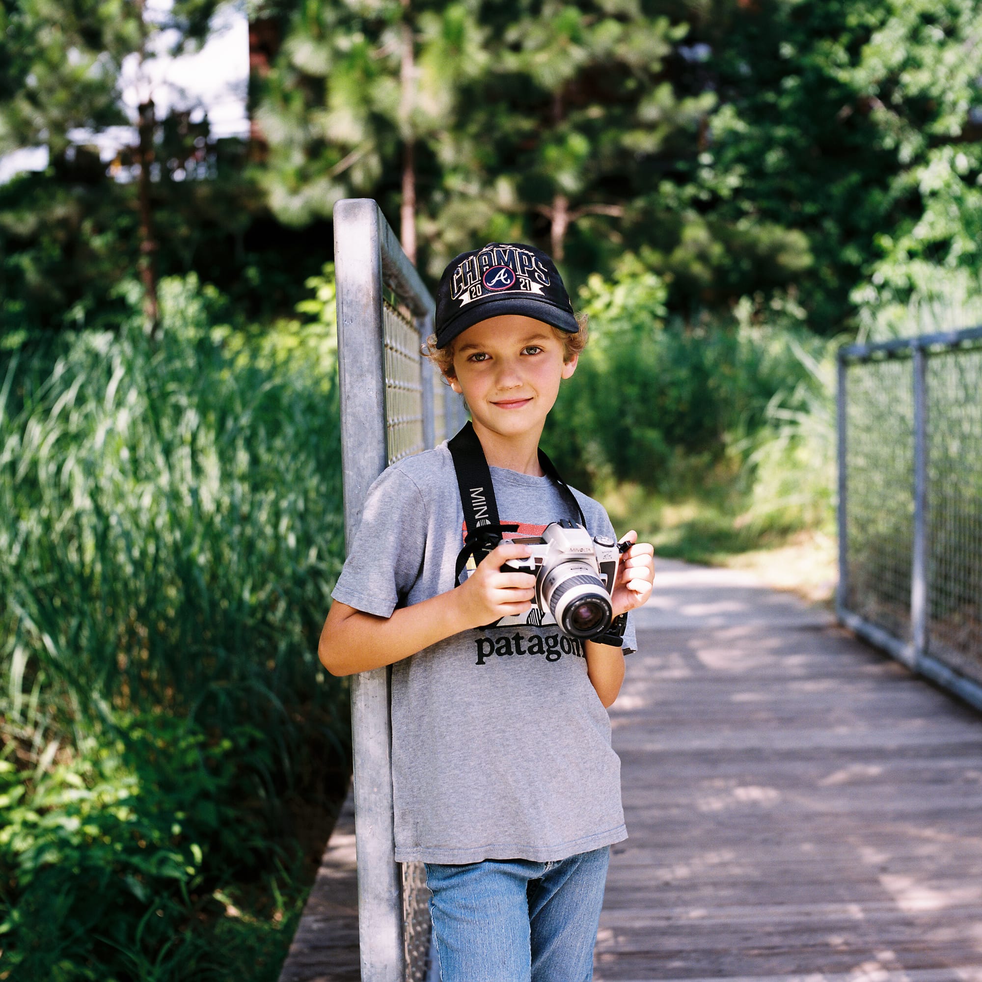A boy standing and holding a camera. He is wearing a Braves hat and a Patagonia shirt.