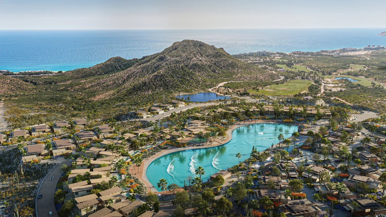 Aerial rendering of Cabo Real upon completion, with a turquoise wave basin surrounded by homes and palms, desert hills, and the ocean beyond