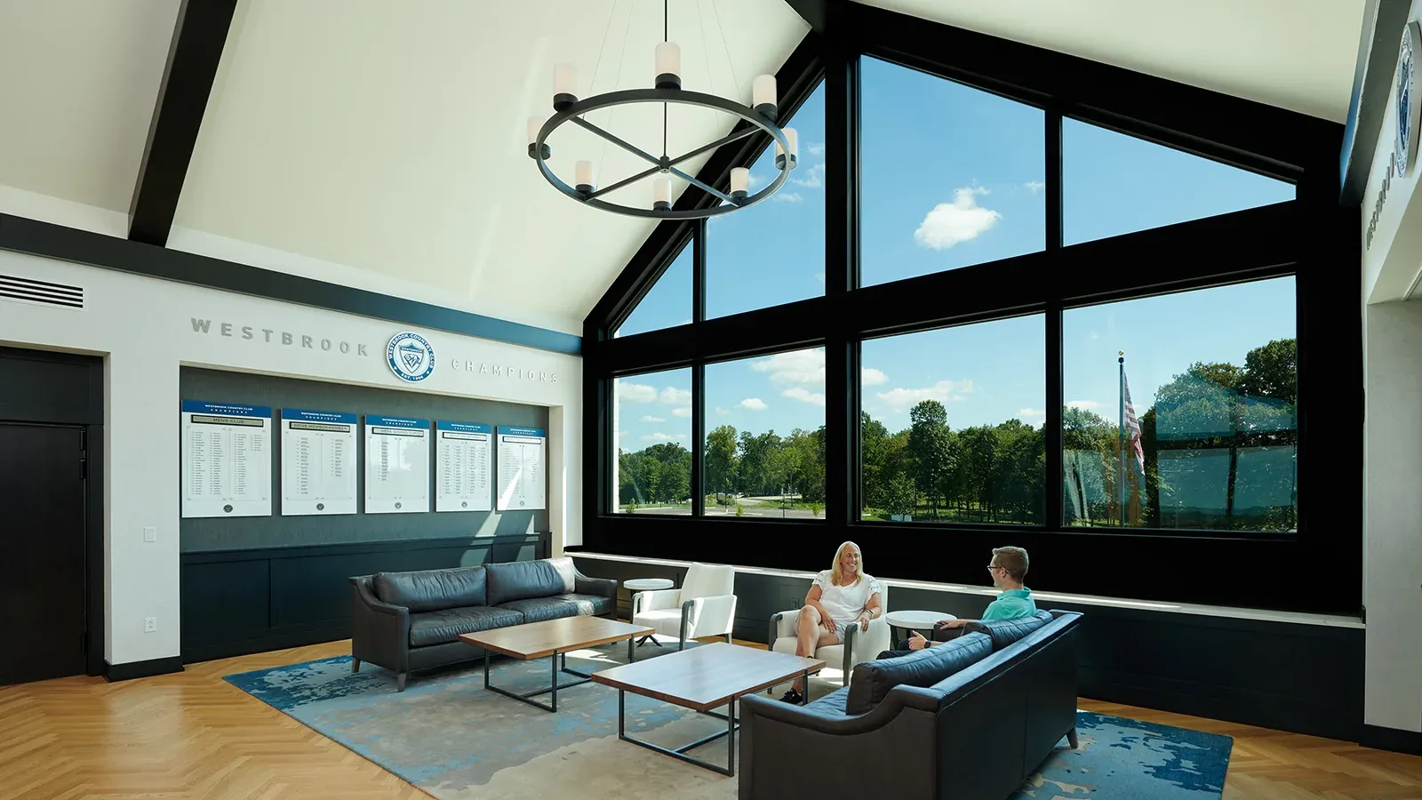 The Champions Lounge, with a gabled wall of windows overlooking the course, leather sofas, and honor boards under a Westbrook Champions sign