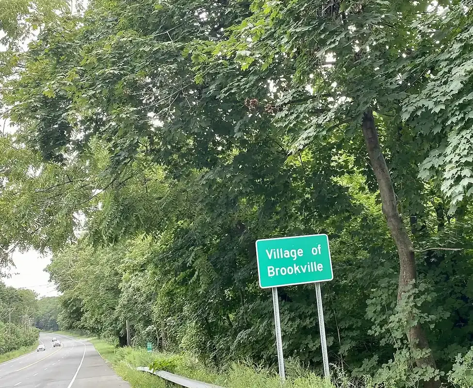 Village of Brookville sign beside a tree-lined road on Long Island, New York