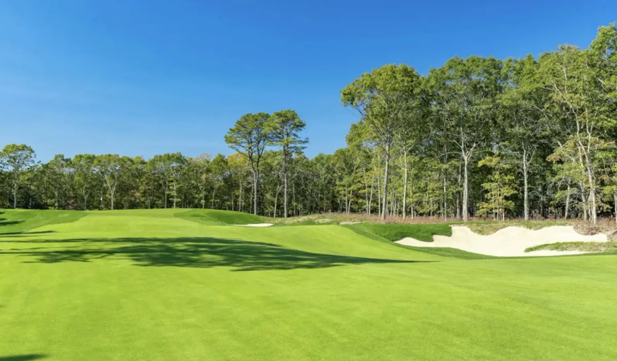 A fairway and white sand bunker framed by pine woods on the Tom Fazio course at The Hills in East Quogue, New York