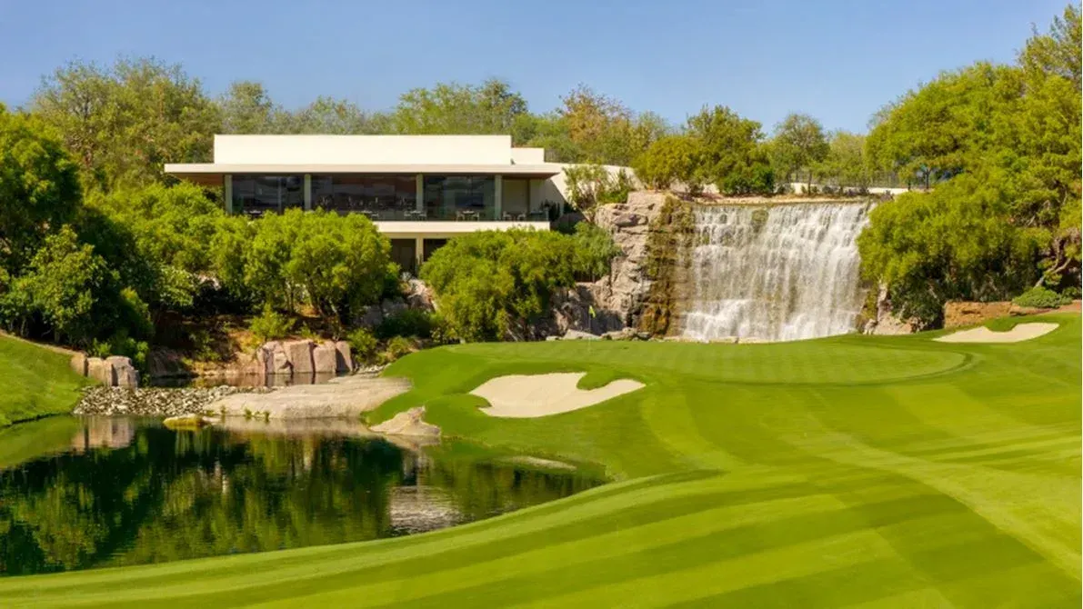 Cliff House, the new two-level clubhouse at Wynn Golf Club in Las Vegas, Nevada, behind the 18th green with a lake in front and a waterfall to the right