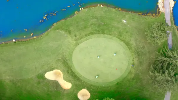 Aerial view looking straight down on a round green with golfers putting, two sand bunkers, and a pond along the fairway at Marion Country Club