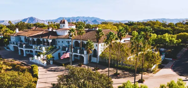 Spanish Hills Club clubhouse exterior with white stucco, tile roof, dome tower, palms, and mountains behind.