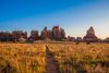 A dirt trail leading through golden grass toward towering red rock spires at Chesler Park Loop Trail in Canyonlands National Park.