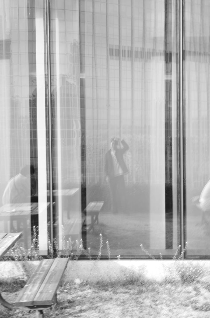 롯데콘서트홀 유리 커튼월에 비친 사람의 실루엣과 빈 벤치, 흑백 사진 · A figure reflected in the glass curtain wall of Lotte Concert Hall, black and white