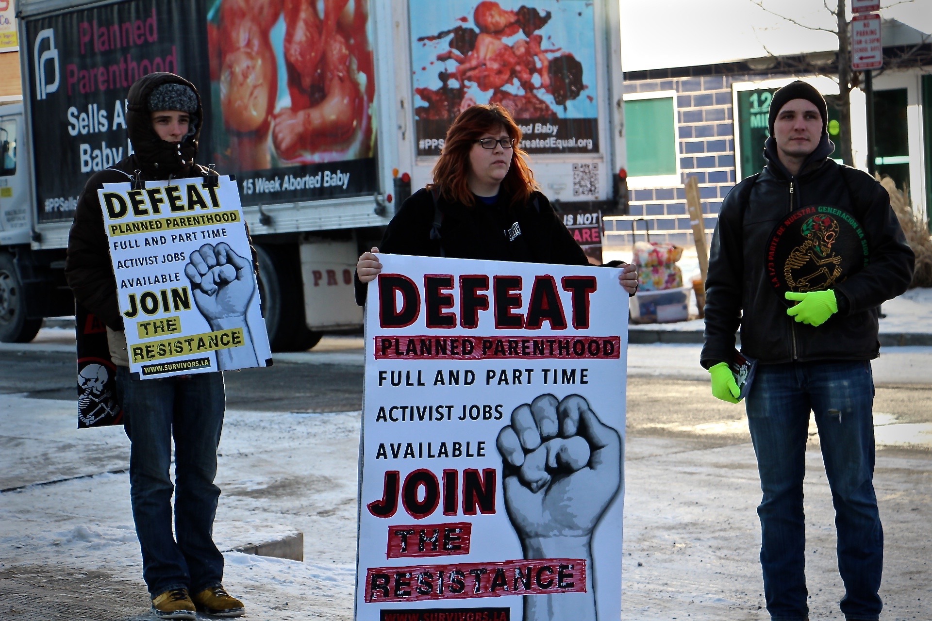 A photograph of anti-abortion activist Lauren Handy, who stands in the center of the image holding a protest sign, flanked on either side by two male protesters.