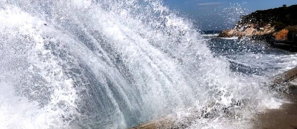 A wave has smashed into a seawall and water is leaping into the air