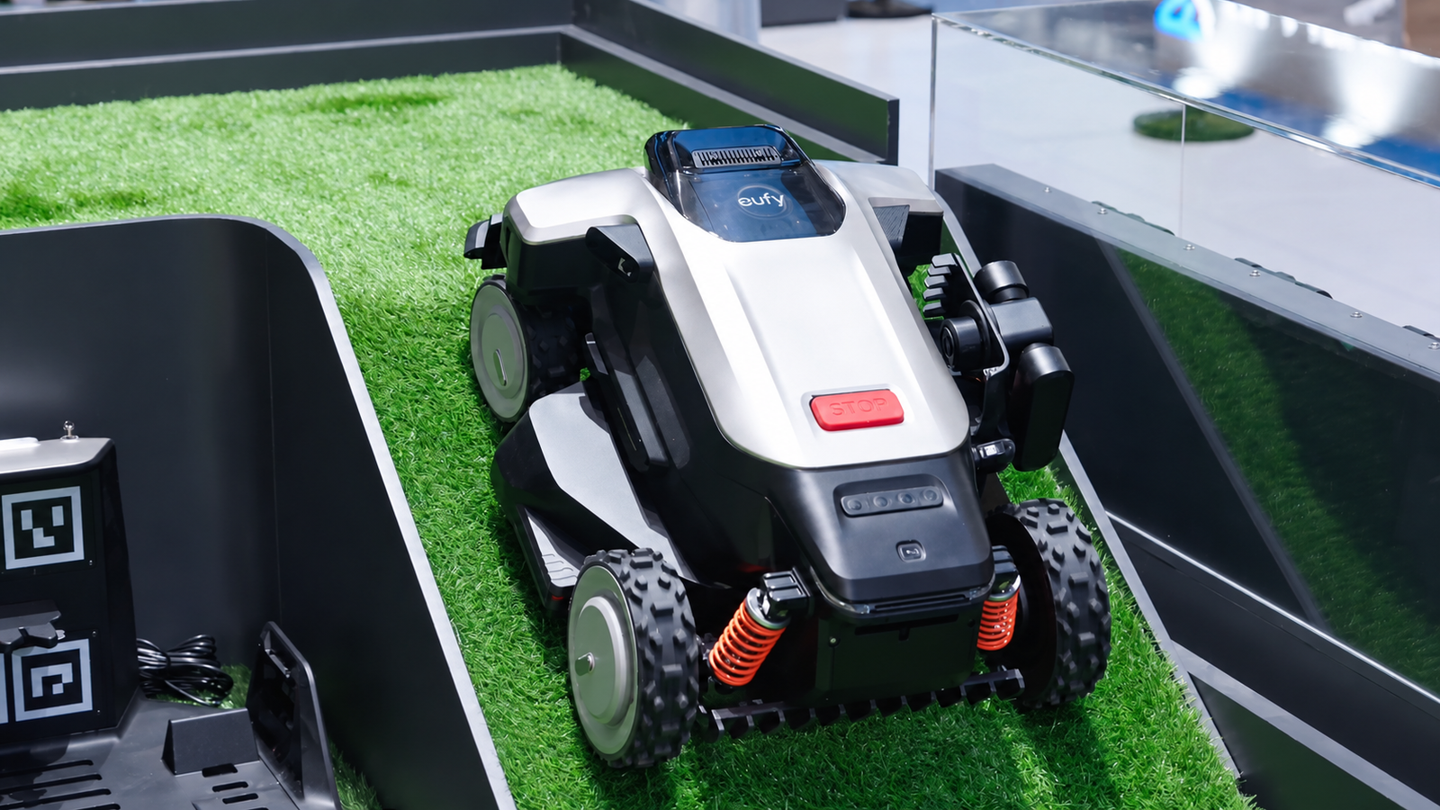 Eufy robot mower displayed on artificial grass at IFA 2026 with four wheels, front suspension and side-mounted hardware.