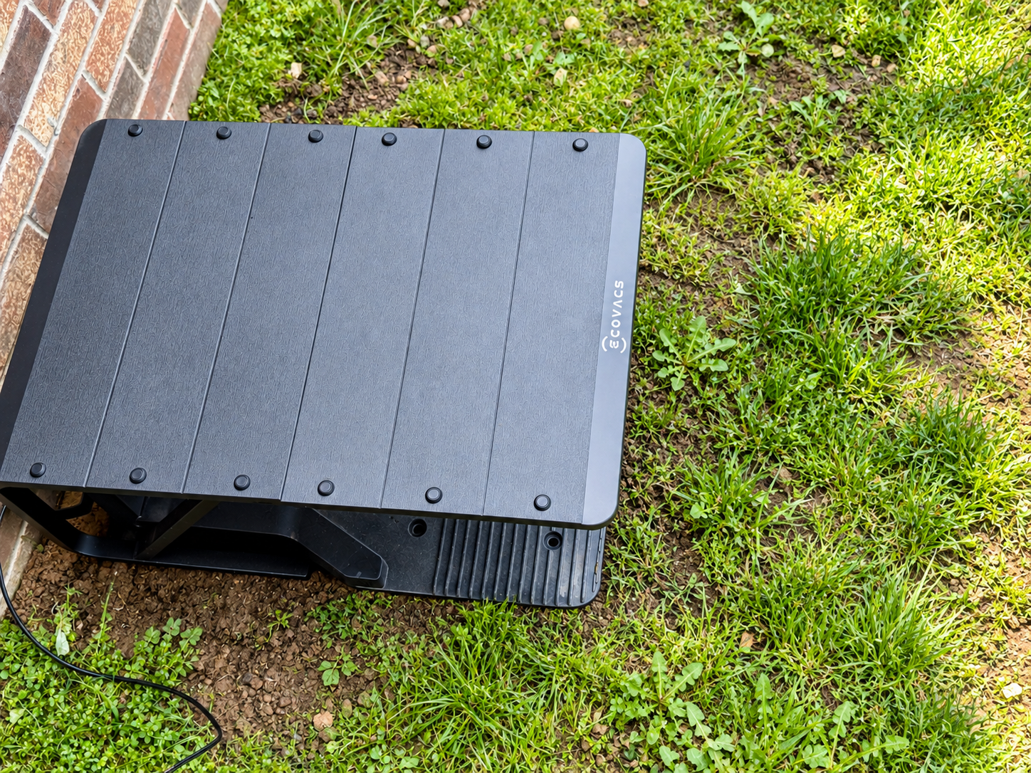 Ecovacs GOAT A2000 LiDAR Pro charging station positioned on grass beside a brick wall. Unboxing collage