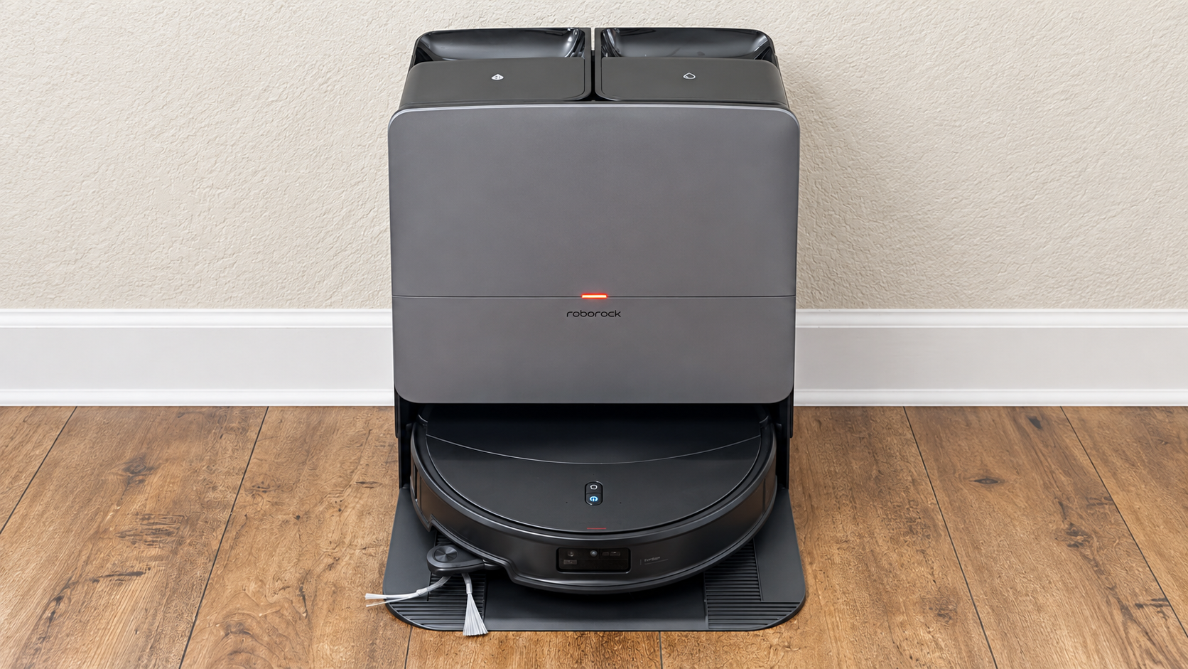 Roborock Saros 20 robot vacuum docked in its gray multifunction station on a hardwood floor.