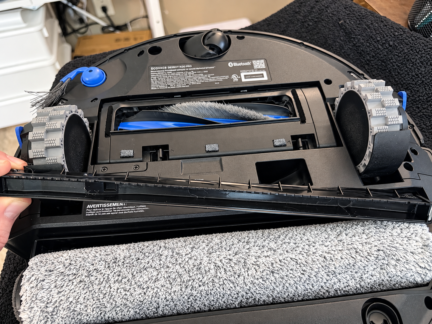 Underside of the Ecovacs Deebot T90 Pro Omni showing the roller mop, main brush, wheels and built-in scraper.