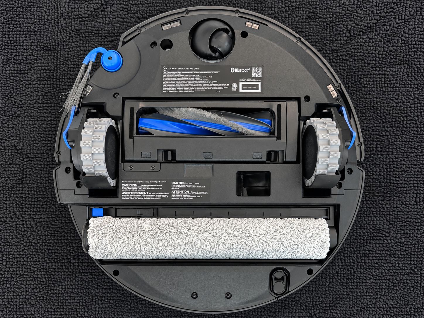 Underside of the Ecovacs Deebot T90 Pro Omni showing the extending side brush, redesigned main brush roller, large drive wheels and full-width Ozmo Roller 3.0 mop.