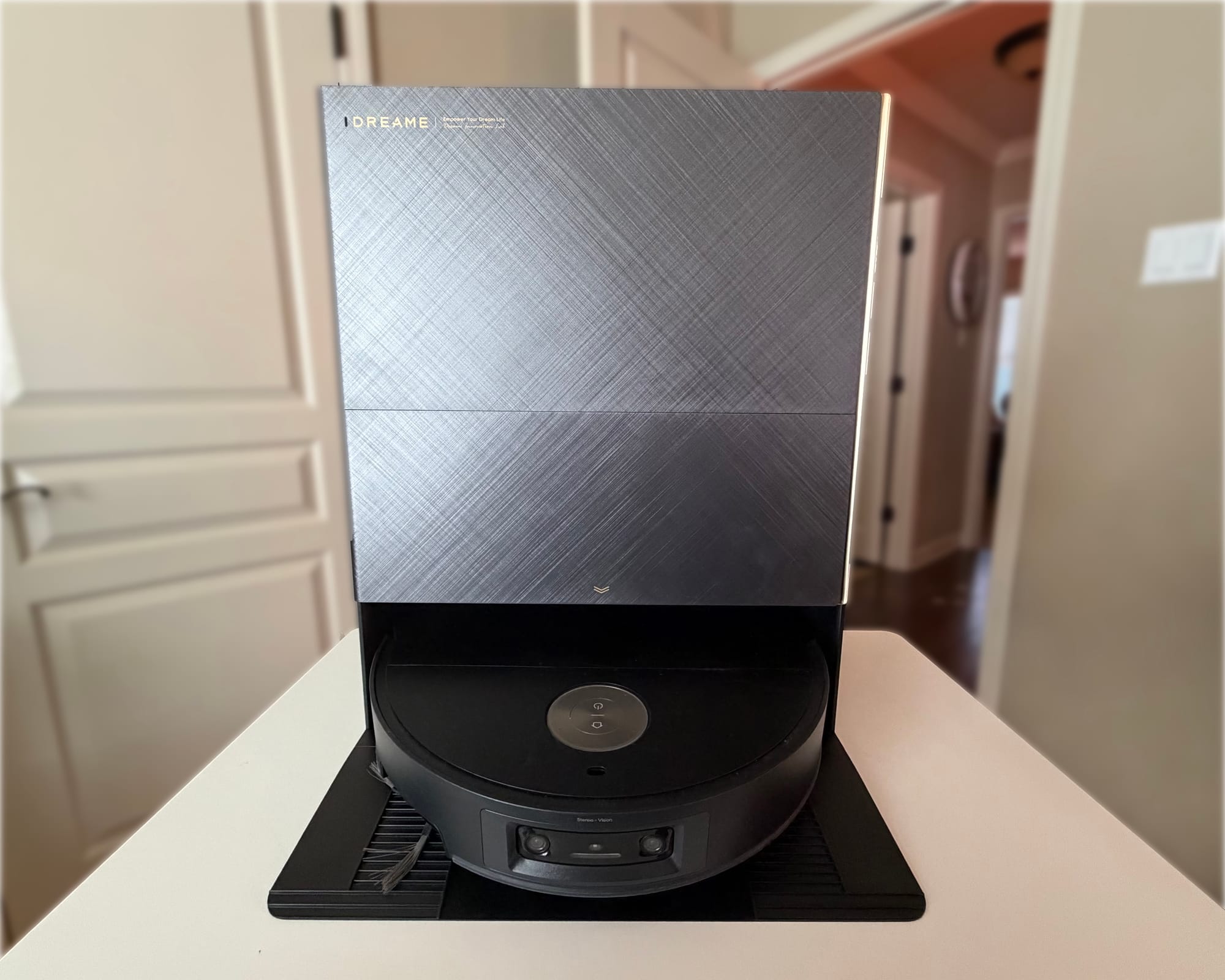 Dreame X60 Ultra robot vacuum in a tall dock with a textured charcoal-gray front, gold accents, and a black base, sitting on a white table.