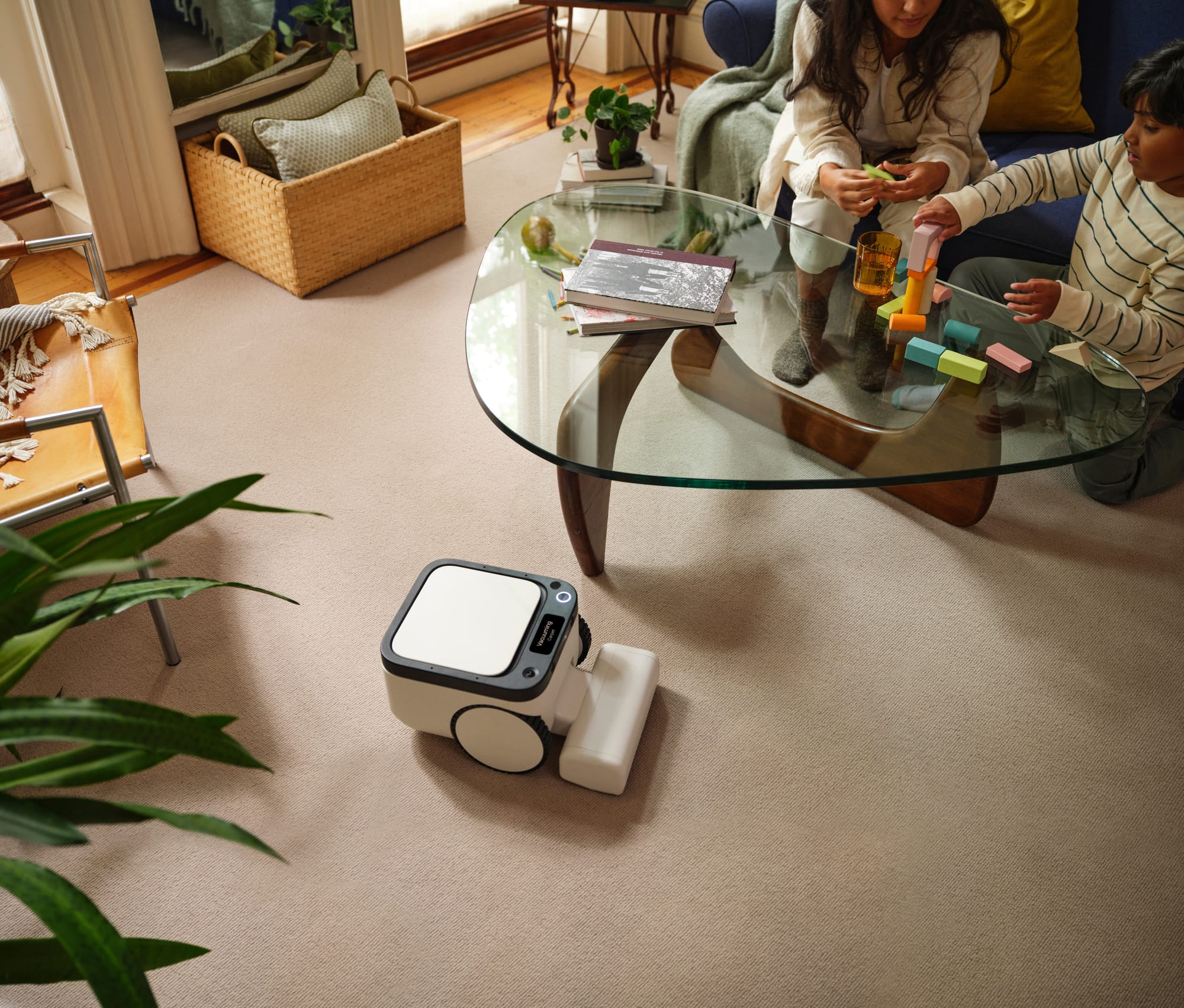 Matic floor-cleaning robot on a beige carpet in a living room while an adult and child sit beside a glass coffee table.
