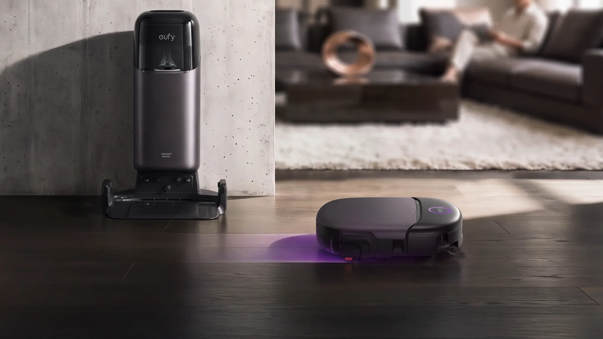 Eufy Omni S2 Pro robot vacuum cleaning a dark hardwood floor with purple UV-C lighting, alongside its multifunction Omni Station.