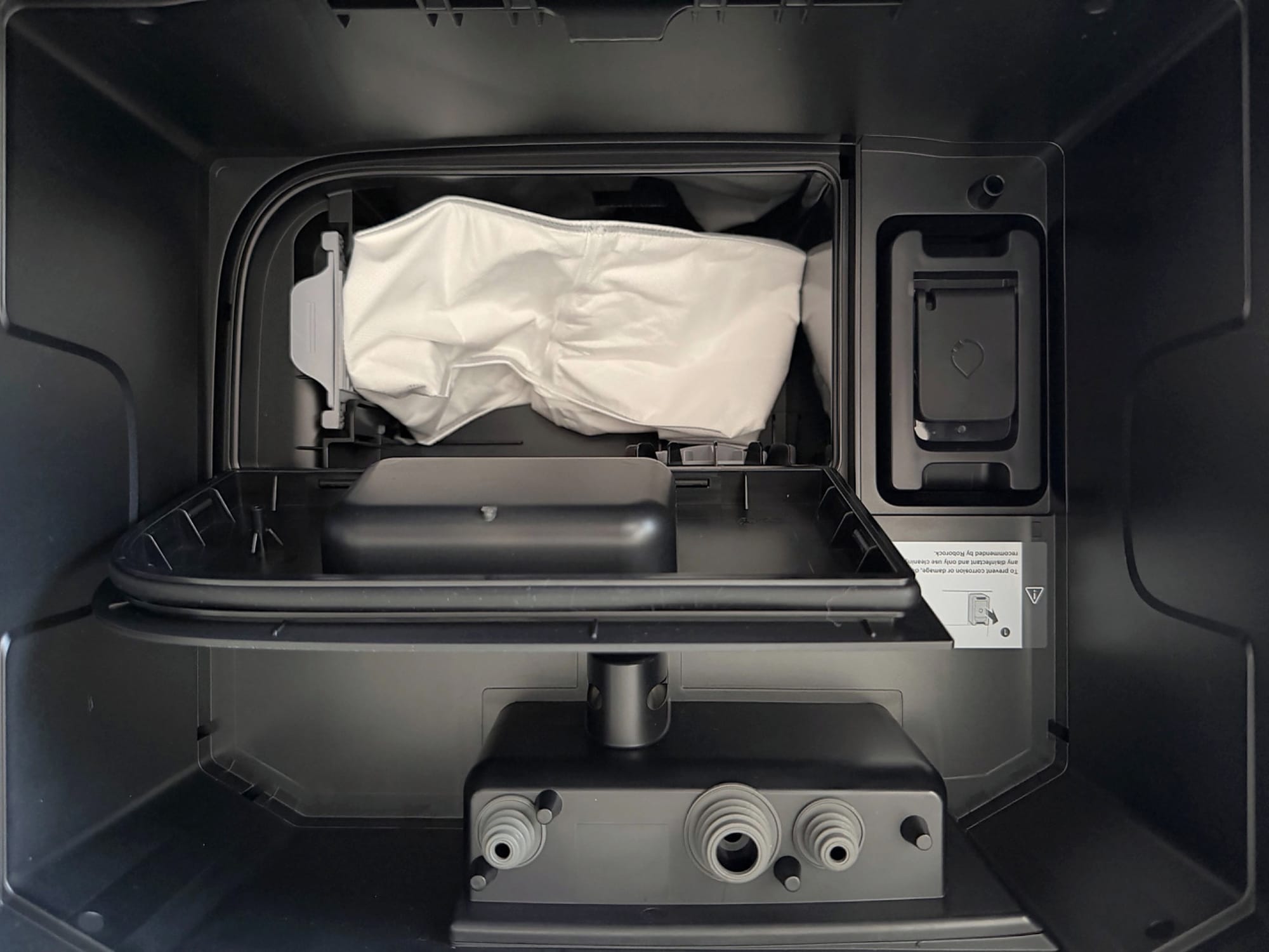 Interior of the Roborock Saros 20 Flow docking station showing a white dust collection bag, cleaning solution compartment and water connections.